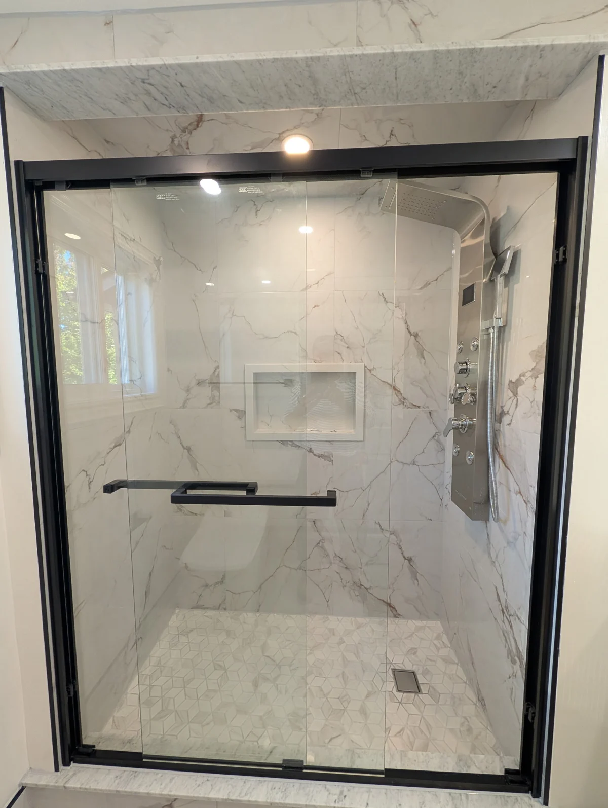 Black-framed glass shower, recessed niche and mosaic shower floor